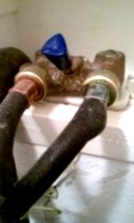 Old metal pipe with blue valve connection and deteriorated fittings showing corrosion and rust